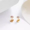 Un par de aretes chapados en oro de 18K con pequeñas piedras preciosas de color púrpura se exhiben sobre un fondo blanco. Hermosas Joyas en Oro Laminado de 18K que agregan un toque de elegancia a cualquier conjunto.