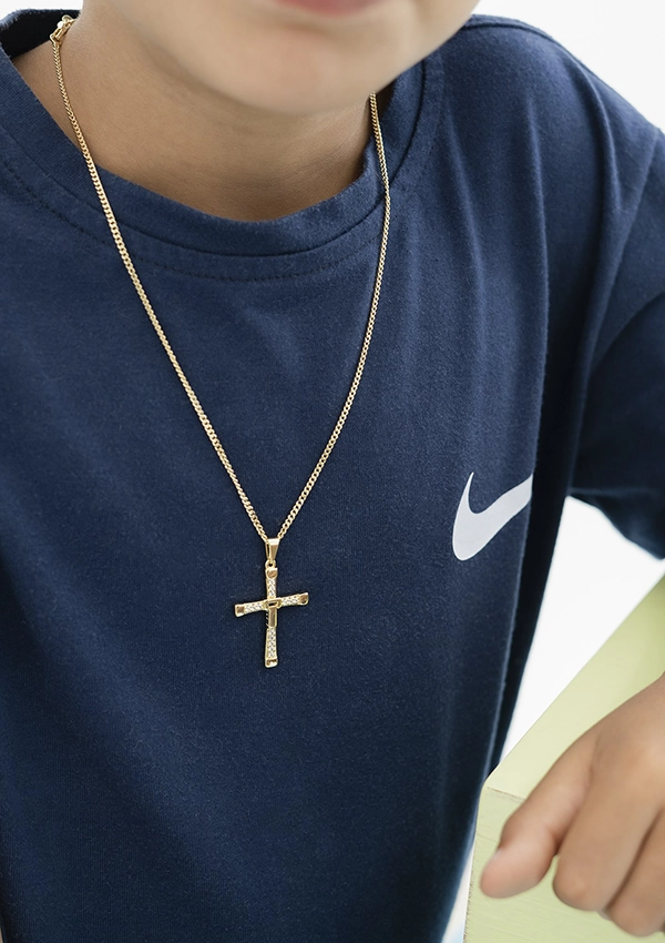 Una persona vistiendo una camisa azul marino con un logo blanco y un collar de cruz de oro de Joyas en Oro Laminado 18K.