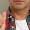 Un hombre vestido con una camisa a cuadros y una camiseta blanca sostiene un colgante de cruz de oro en un collar, mostrando la elegancia de Joyas en Oro Laminado 18K.