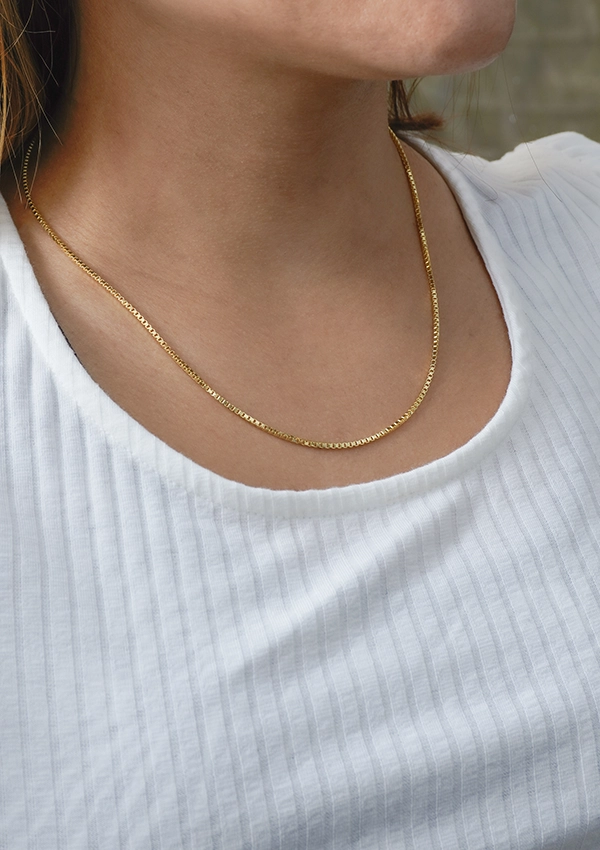 Persona que lleva una camisa blanca acanalada y un impresionante collar de cadena de oro elaborado con Joyas en Oro Laminado de 18K, con el collar apoyado plano sobre la parte superior del pecho.