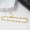 Pulsera de oro y perlas con cadena ajustable expuesta sobre una superficie blanca junto a contenedores con formas geométricas.