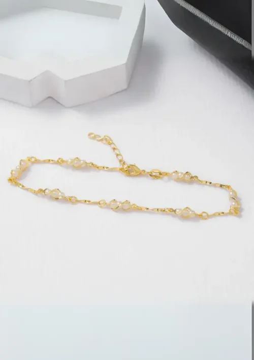 Una delicada pulsera de oro con perlas sobre una superficie blanca.