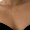 Una mujer luce el Dije Diamante, un collar de oro con un colgante geométrico, resaltado sobre un top negro sin tirantes.