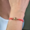 Una persona que lleva una Pulsera San Benito Tradicional herraje pequeño, con un diseño trenzado rojo con un pequeño medallón dorado en su muñeca.