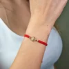 Una persona lleva la Pulsera San Benito Tradicional herraje pequeño, que muestra su pequeño medallón dorado en la muñeca. Está vestida con una blusa blanca.