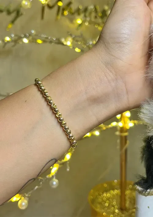 Una mano adornada con la Pulsera Full Balín liso e italiano dorado de 0,4 milímetros, sobre un fondo de luces de cadena.