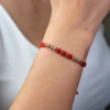 Primer plano del brazo de una persona que lleva la Pulsera Infinito, con cuentas rojas y detalles de metal, sobre una parte superior blanca.