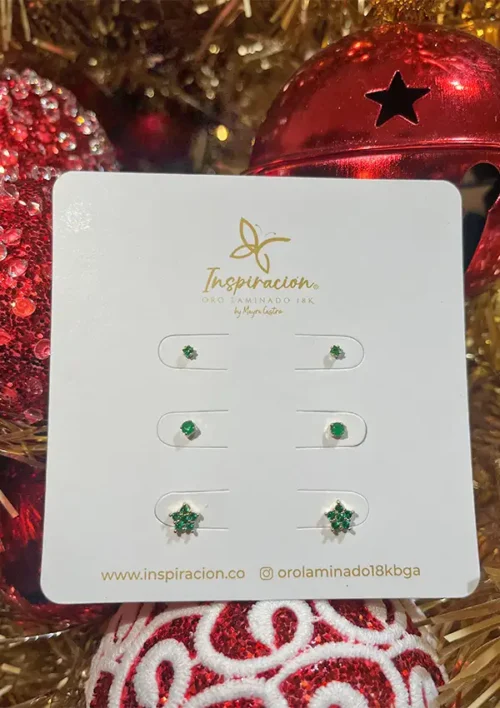 Un conjunto de pendientes "Sets Aretes Verdes" se muestra en una tarjeta con adornos navideños rojos de fondo.