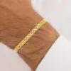 Primer plano de la muñeca de una persona que lleva una pulsera de cadena de oro sobre un fondo claro.