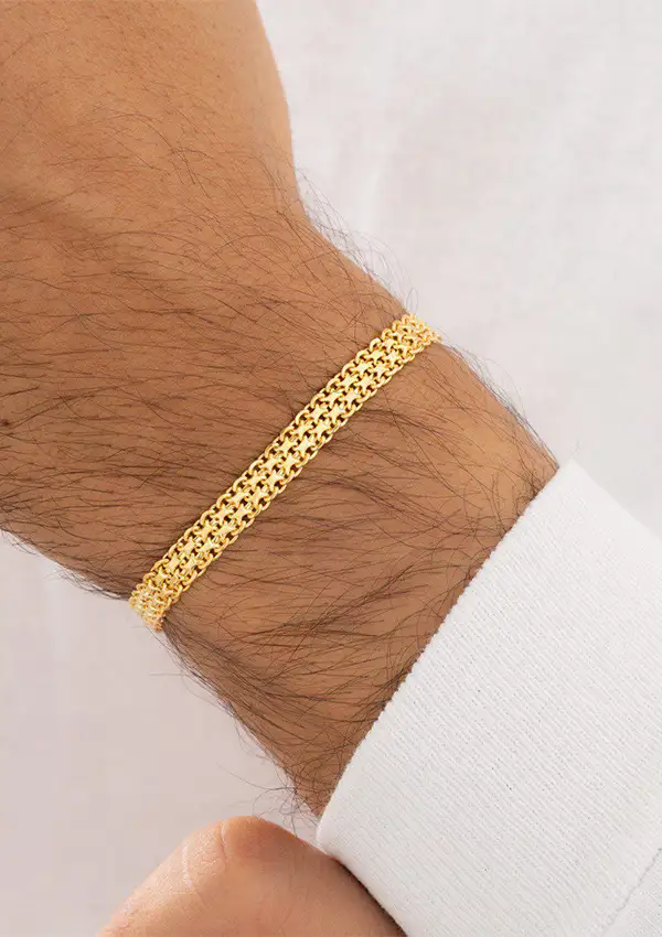 Primer plano de la muñeca de una persona que lleva una pulsera de cadena de oro sobre un fondo claro.