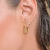 Primer plano de la oreja de una mujer adornada con un aro de oro Candonga mini C. de 8 mm y un pendiente de puño de oro con pequeñas piedras en la parte superior de la oreja; el cabello está recogido.