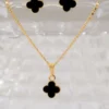 Conjunto Aretes y dije Clover Negro 1cm exhibido en un soporte transparente, presenta un conjunto de joyas de oro con un colgante en forma de trébol negro y aretes a juego.