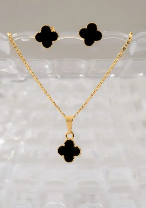 Conjunto Aretes y dije Clover Negro 1cm exhibido en un soporte transparente, presenta un conjunto de joyas de oro con un colgante en forma de trébol negro y aretes a juego.