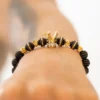 Primer plano de una muñeca con la pulsera Herraje Corona, que muestra cuentas negras y detalles dorados con un dije de corona dorada central.