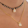 Dos collares con colgantes cuadrados: el de arriba tiene cuentas negras y el de abajo es una cadena dorada. Producto: Dije Escapulario San Benito.