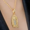 El Dije Nuestra Señora de Guadalupe circonias es un collar de oro con un colgante ovalado grabado con una figura, que se lleva elegantemente sobre tela oscura.