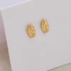 Los Aretes Guadalupe Finita son unos aretes ovalados de oro que presentan un diseño de figura religiosa, elegantemente presentados sobre una tarjeta blanca.